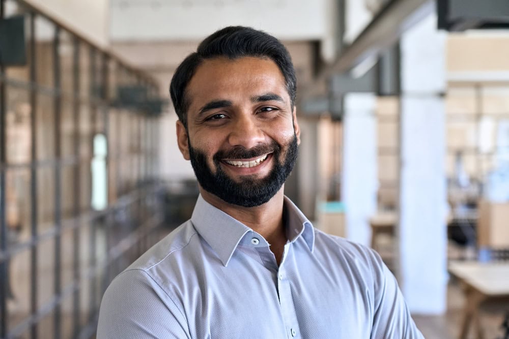 Happy smiling bearded indian business man small business owner, company leader or sales manager, male hispanic ceo executive, successful lawyer looking at camera standing in office, headshot portrait.