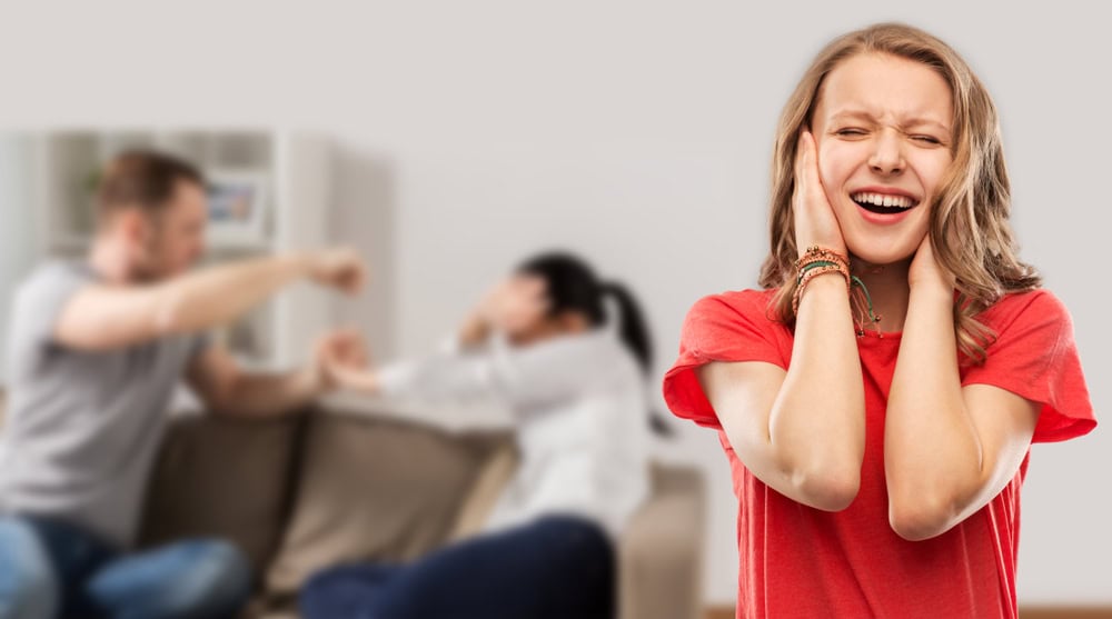 domestic violence, assault and social issue concept - unhappy stressed teenage girl covering her ears when her mother and father having fight background