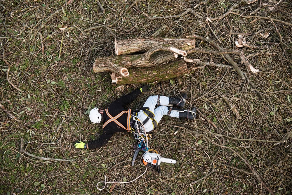 Injured lumberjack with chainsaw lying on the ground after fall